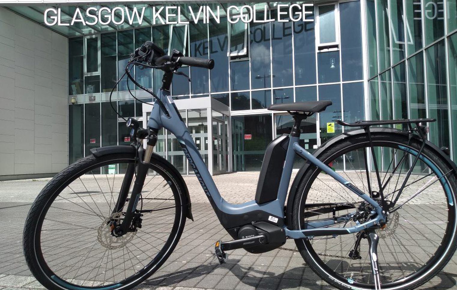 Electric bike parked outside the glass entrance of Glasgow Kelvin College Springburn campus.