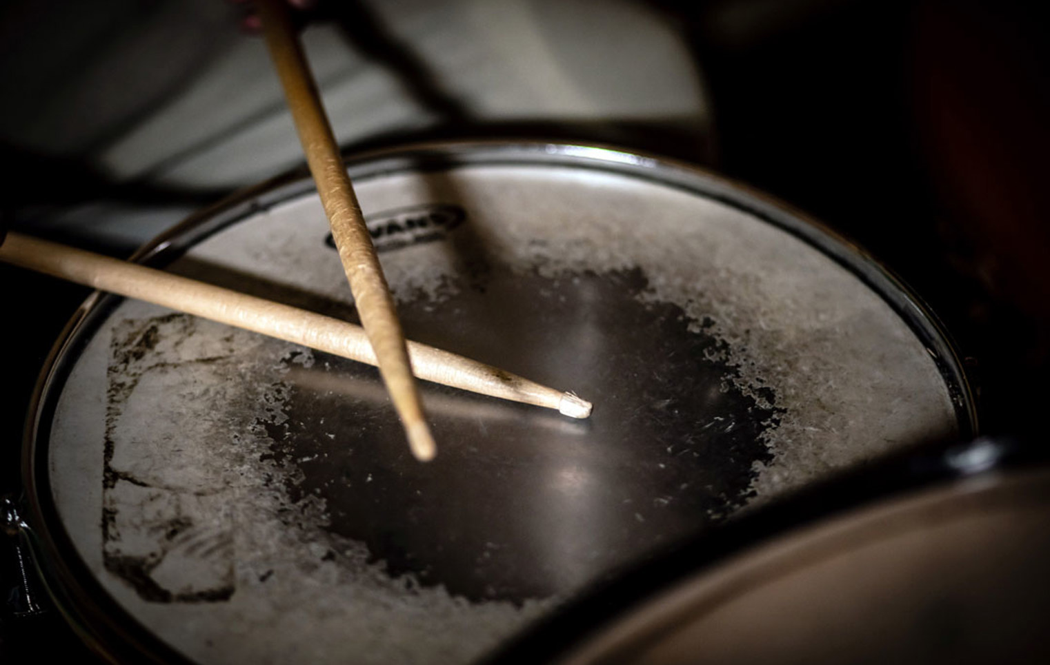A pair of wooden drumsticks resting on a worn snare drum surface, showing signs of frequent use.