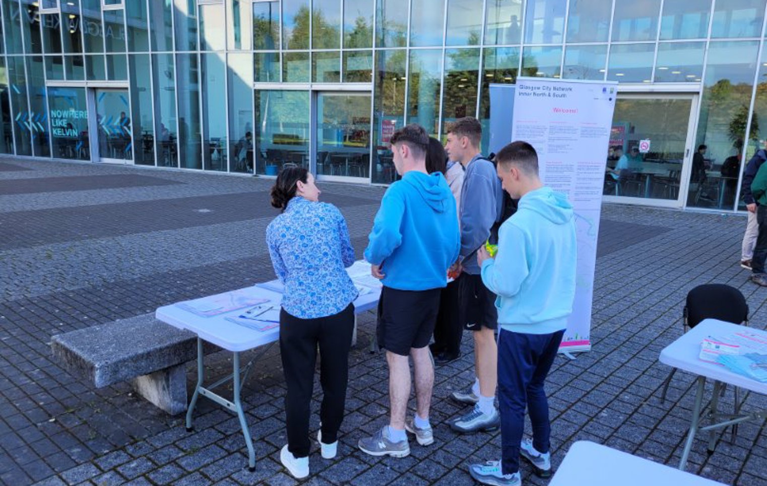 Glasgow Kelvin College students and staff gathered around an information table outside the campus building, exploring new active travel network maps and resources.
