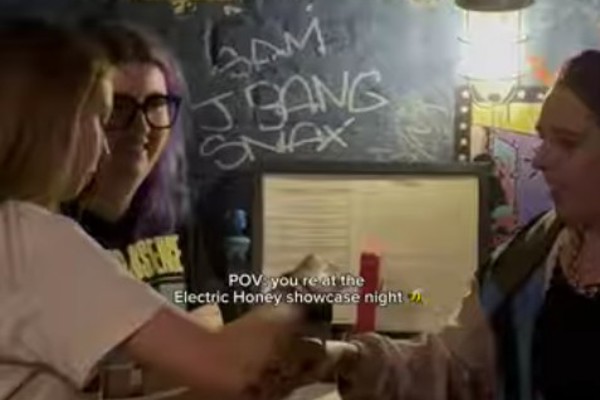 Students welcoming guests at the Electric Honey showcase night, standing behind a merch table at Stereo in Glasgow.