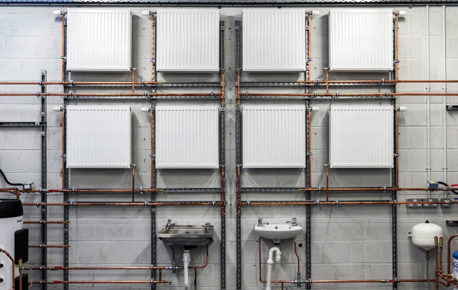Wall-mounted radiators, sinks, and copper pipework arranged in a plumbing training workshop at Glasgow Kelvin College