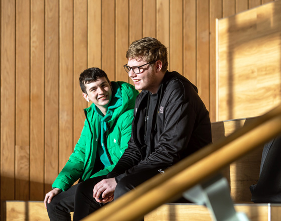 Two students sitting on tiered wooden seating at Springburn campus, chatting and enjoying the sunlight.