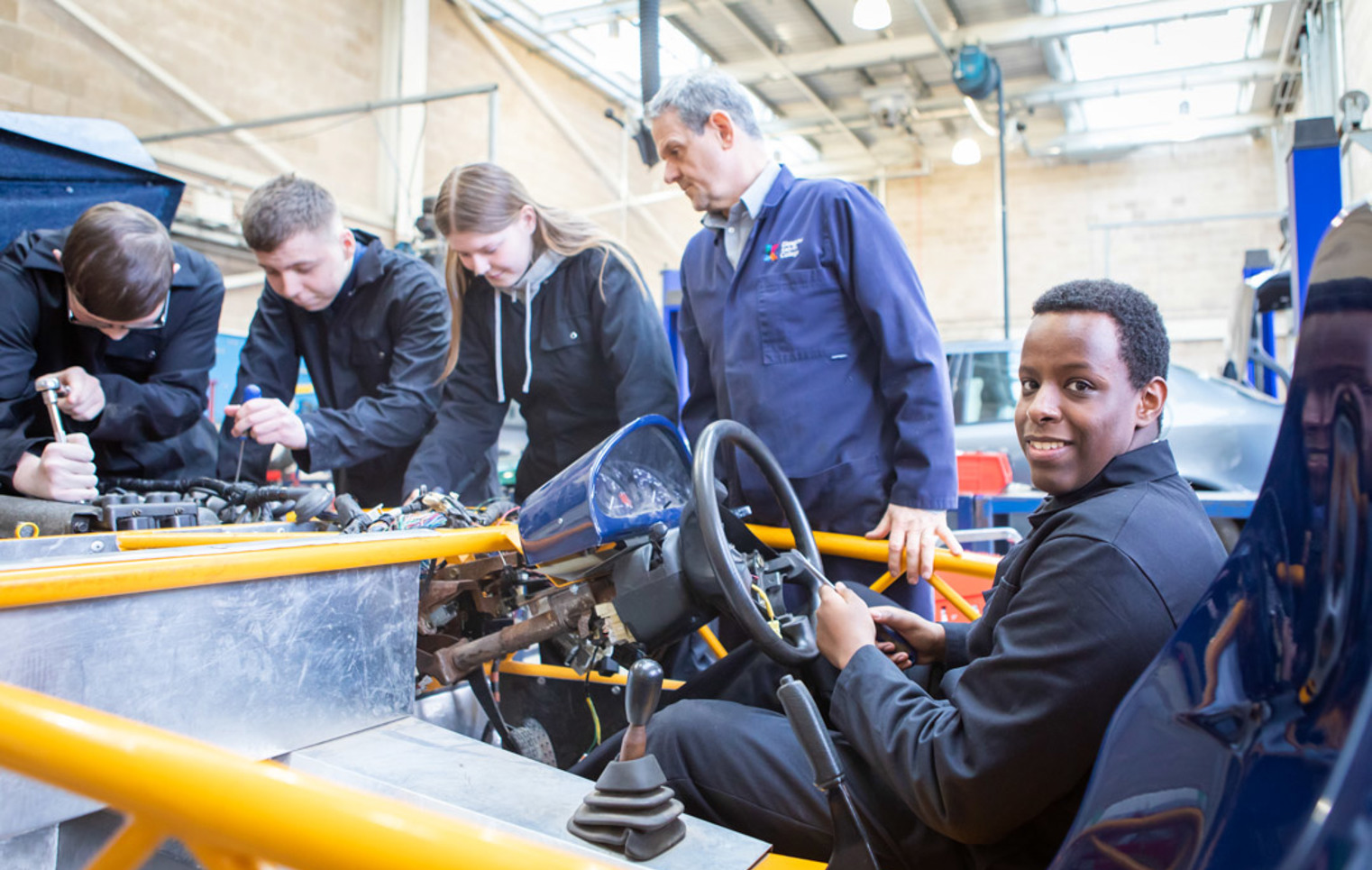 Instructor and students collaborating on an engine repair project, focusing on mechanical details in a hands-on learning session.