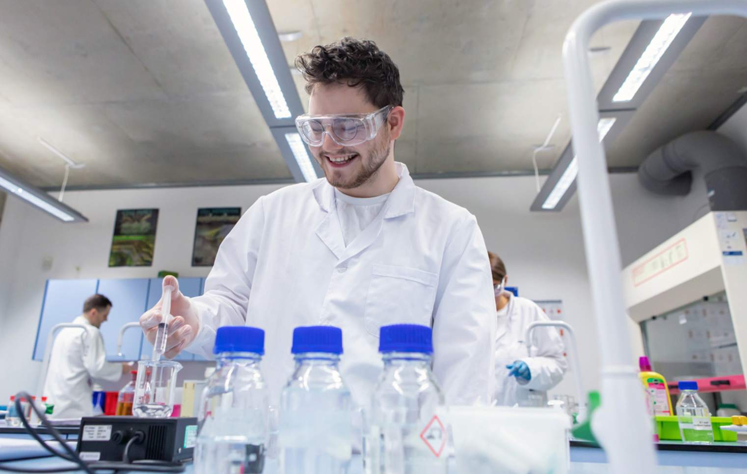 Male student wearing lab coat and goggles pipetting liquid during science experiment
