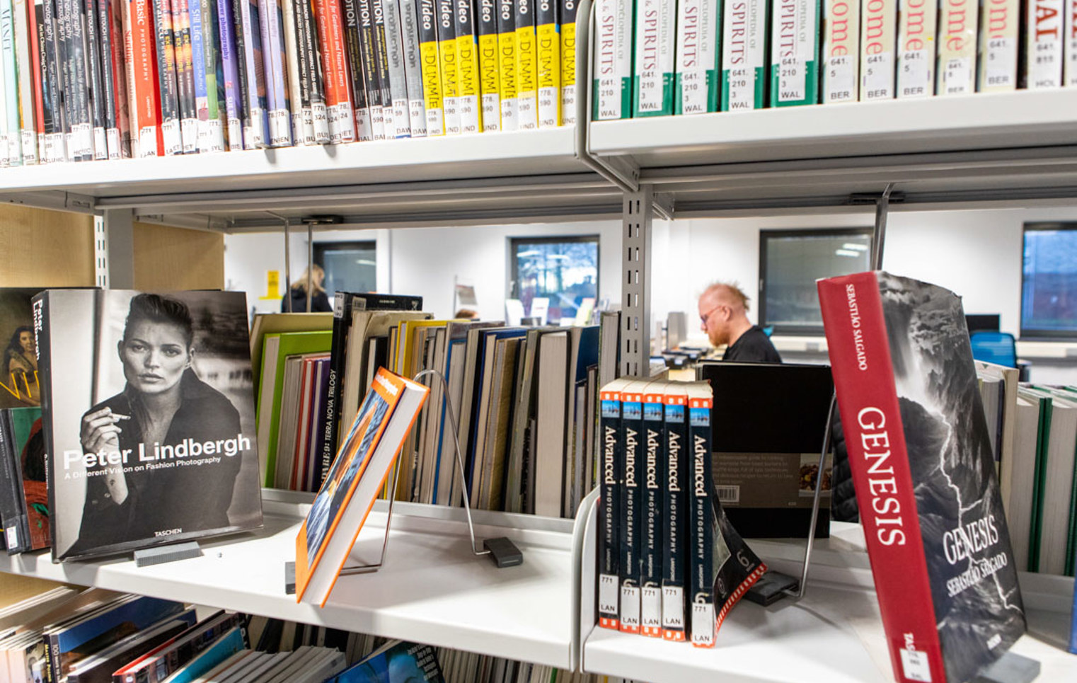 Books on display in the Easterhouse Campus library at Glasgow Kelvin College, with a student working in the background.
