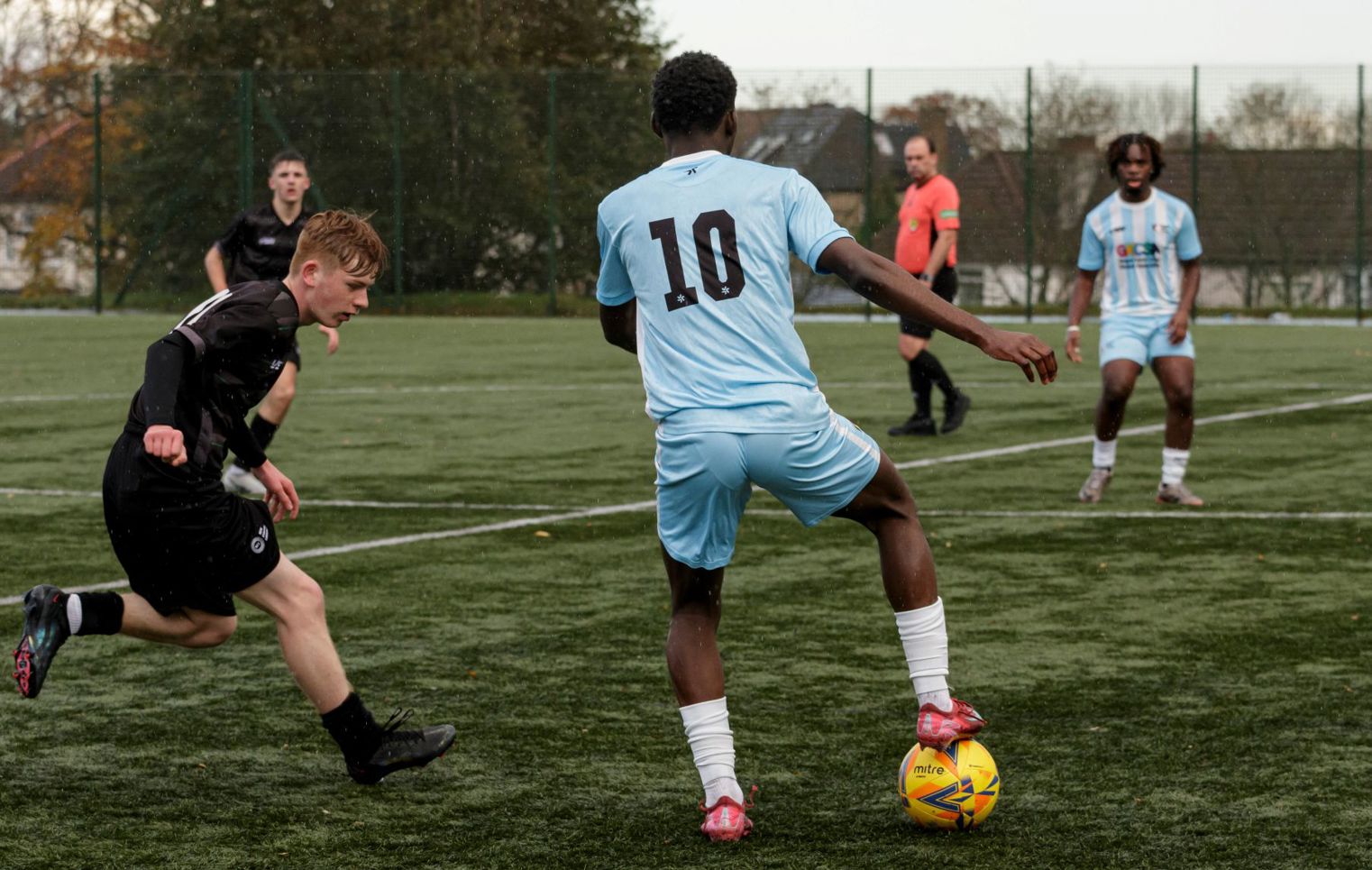Glasgow Kelvin College football player in light blue kit controlling the ball during a competitive match on an outdoor pitch.