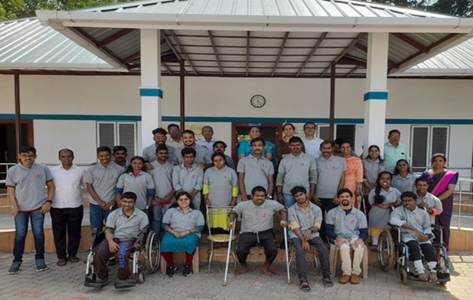 Group photo of staff and youth with disabilities outside a building at IOCL Kerala, with some individuals seated in wheelchairs and others standing, all smiling.