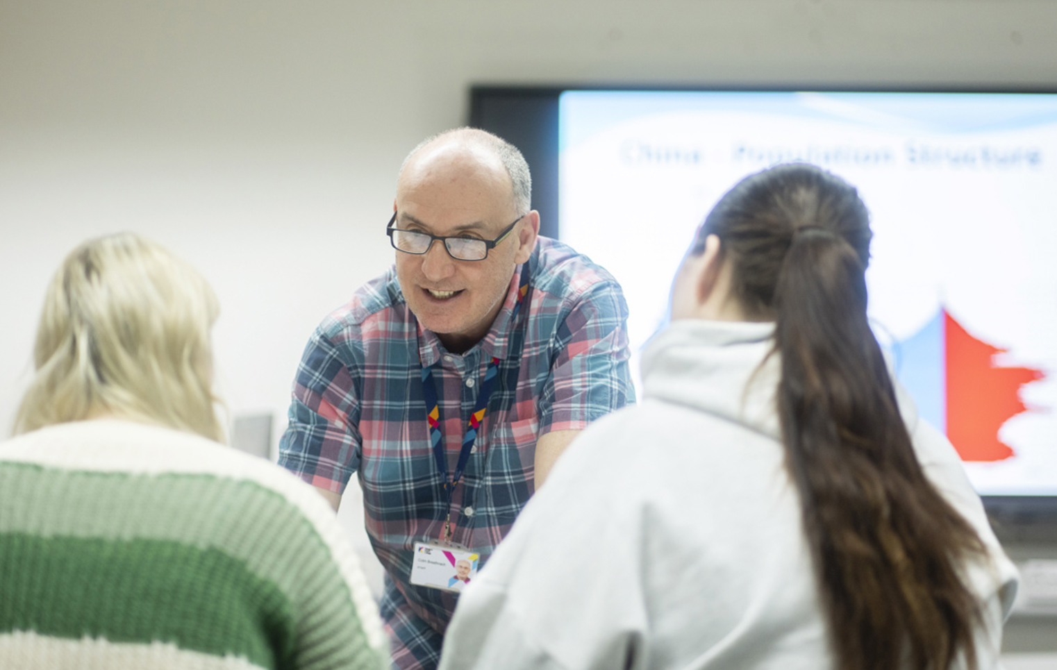 Smiling lecturer interacts closely with two students during a class at Glasgow Kelvin College.