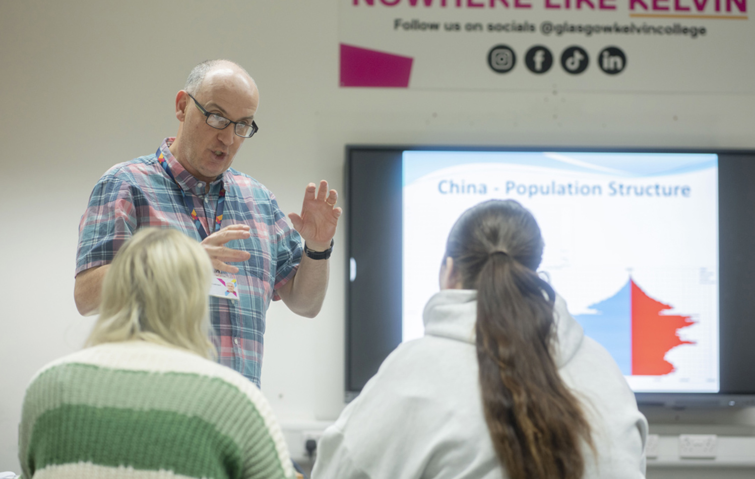 Lecturer speaks to students during a session on population structure, under a “Nowhere Like Kelvin” sign.