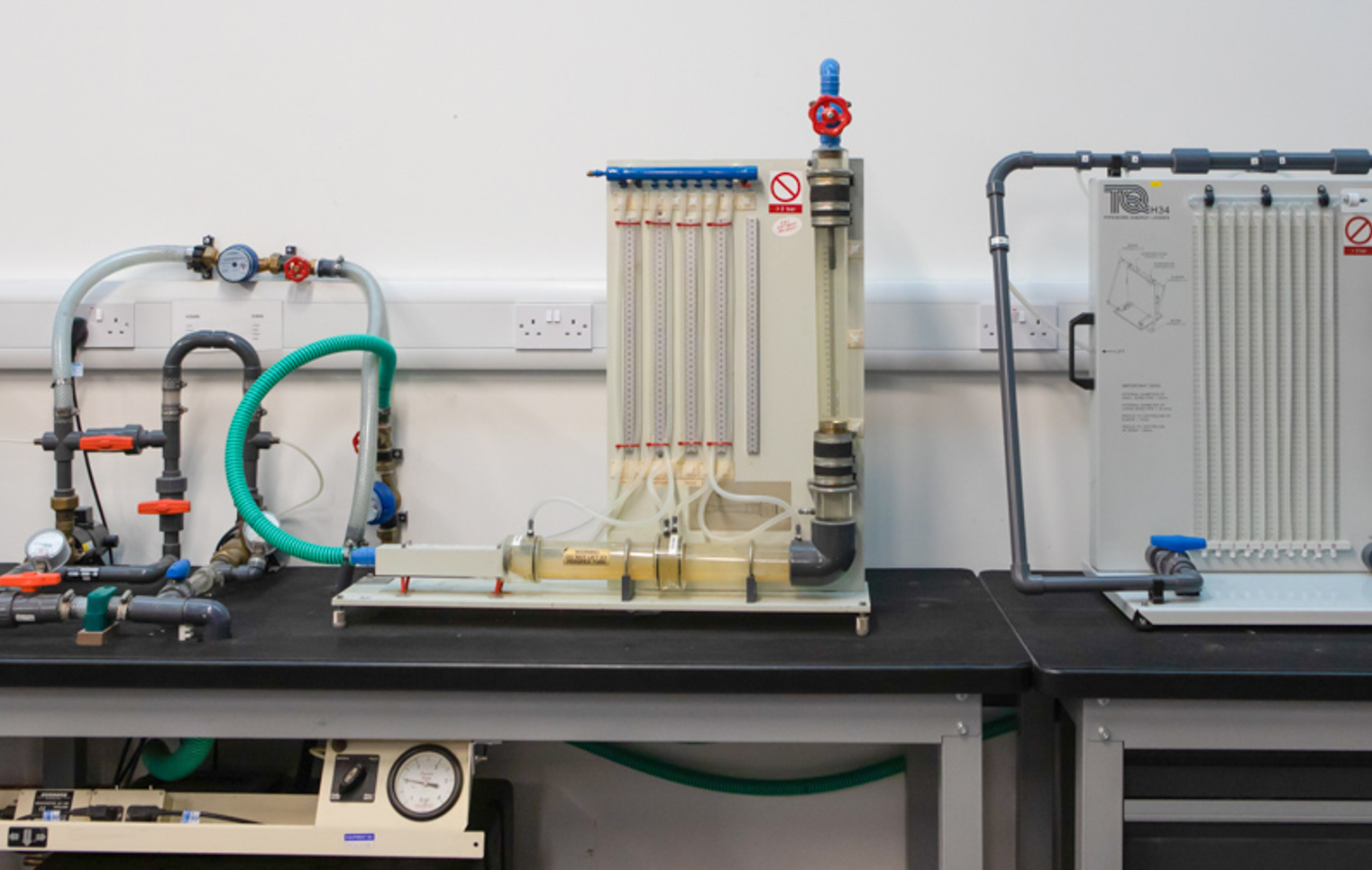 A set of fluid mechanics training rigs with interconnected pipes, valves, and flow meters, used for hands-on learning in a building services workshop.