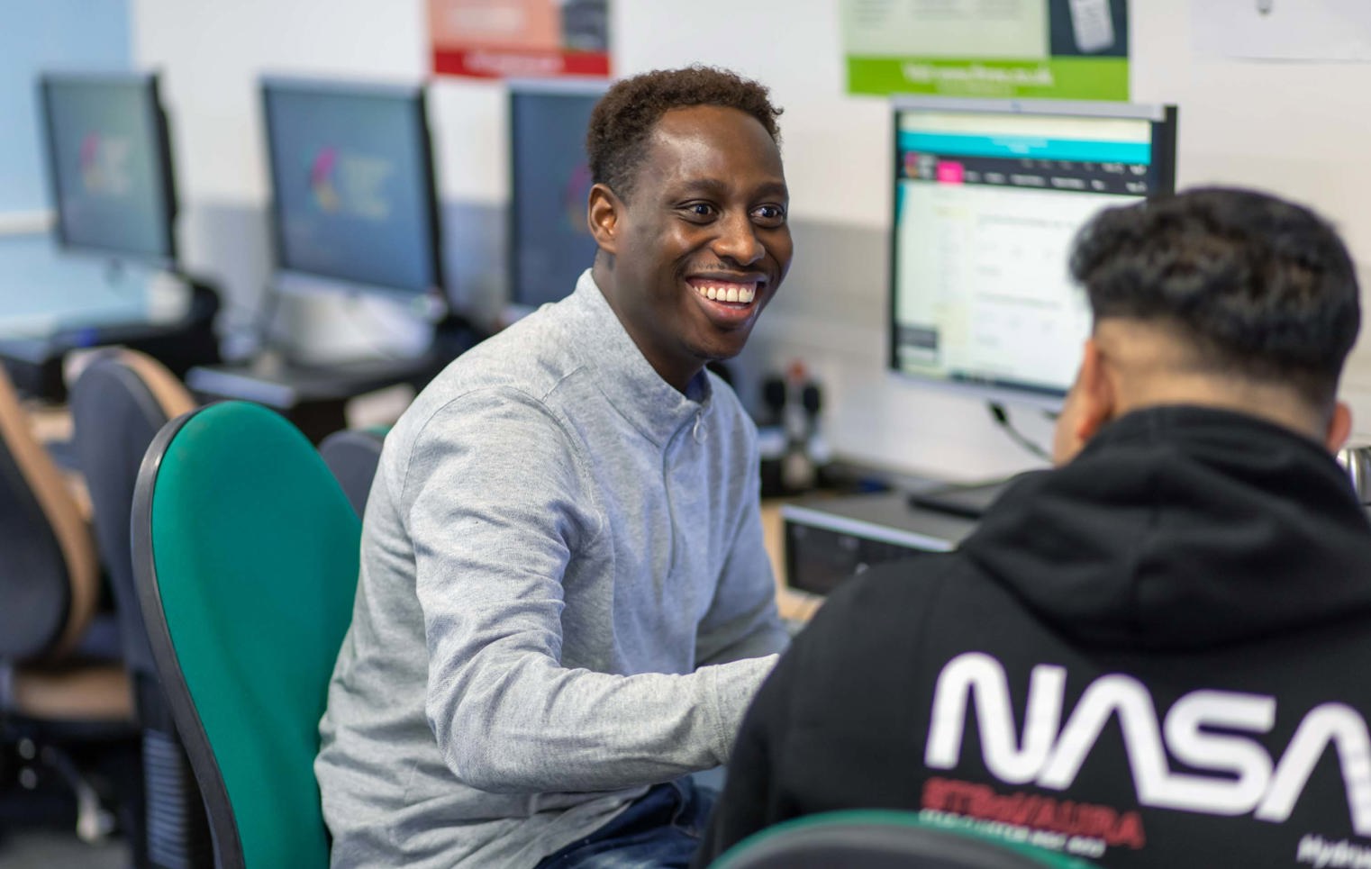 Two students working together at a computer in a business and administration course, one smiling while engaged in discussion.