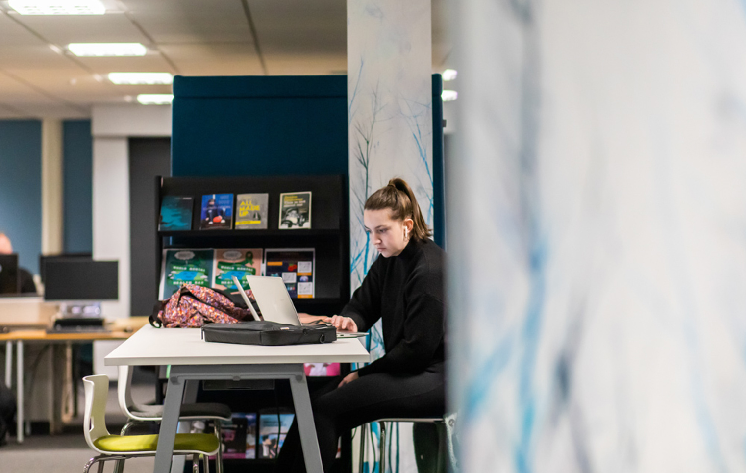 Student working on a laptop at a study desk in the Library and Flexible Learning Centre at Glasgow Kelvin College’s Easterhouse Campus, with bookshelves and resources in the background.