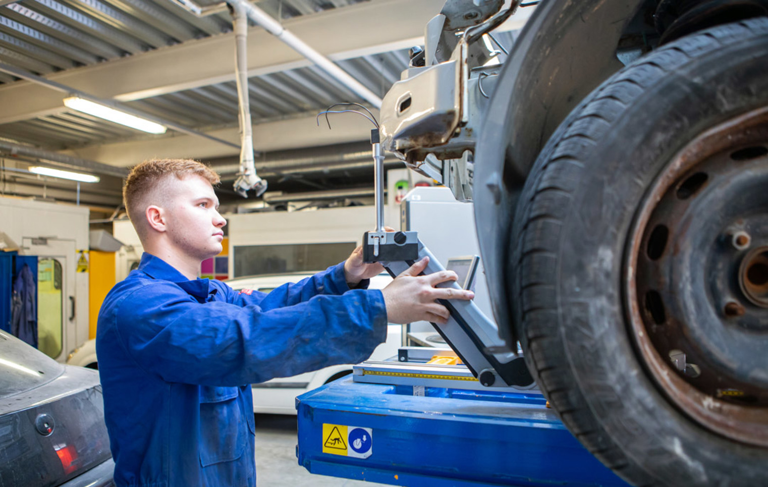 Automotive student adjusting alignment tools on a raised vehicle during a practical class.