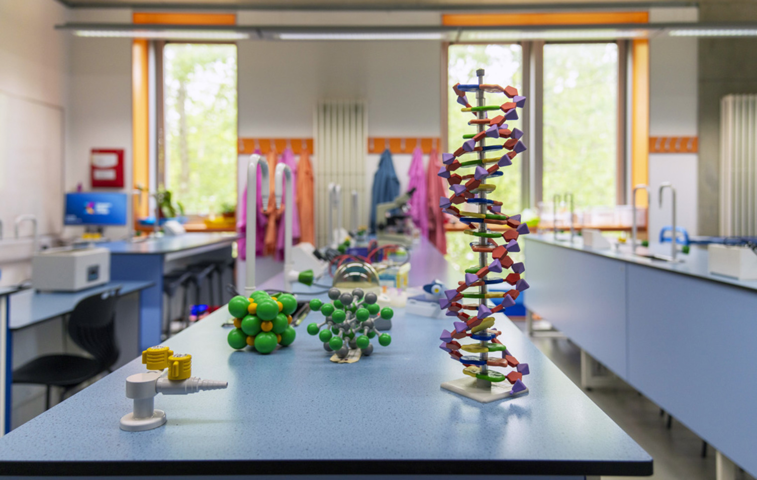 A bright science lab with colourful lab coats hanging by the windows, a tall DNA model standing proudly on the bench, and lots of molecule models ready for some hands-on experiments and creative discovery