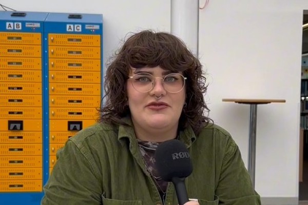 Digital Design student Georgia speaking on camera about her experience at Glasgow Kelvin College, seated at a table with lockers in the background.