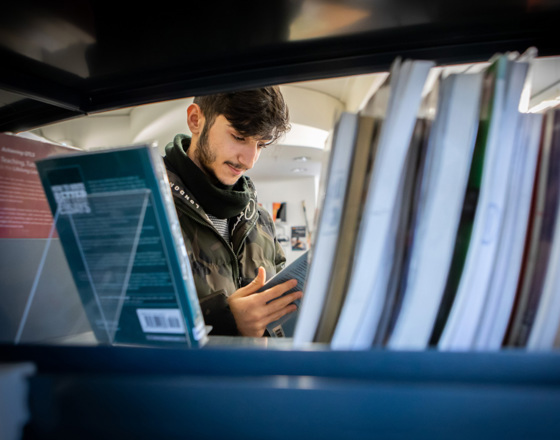 Student browsing and reading a book between shelves in the East End Campus library at Glasgow Kelvin College.