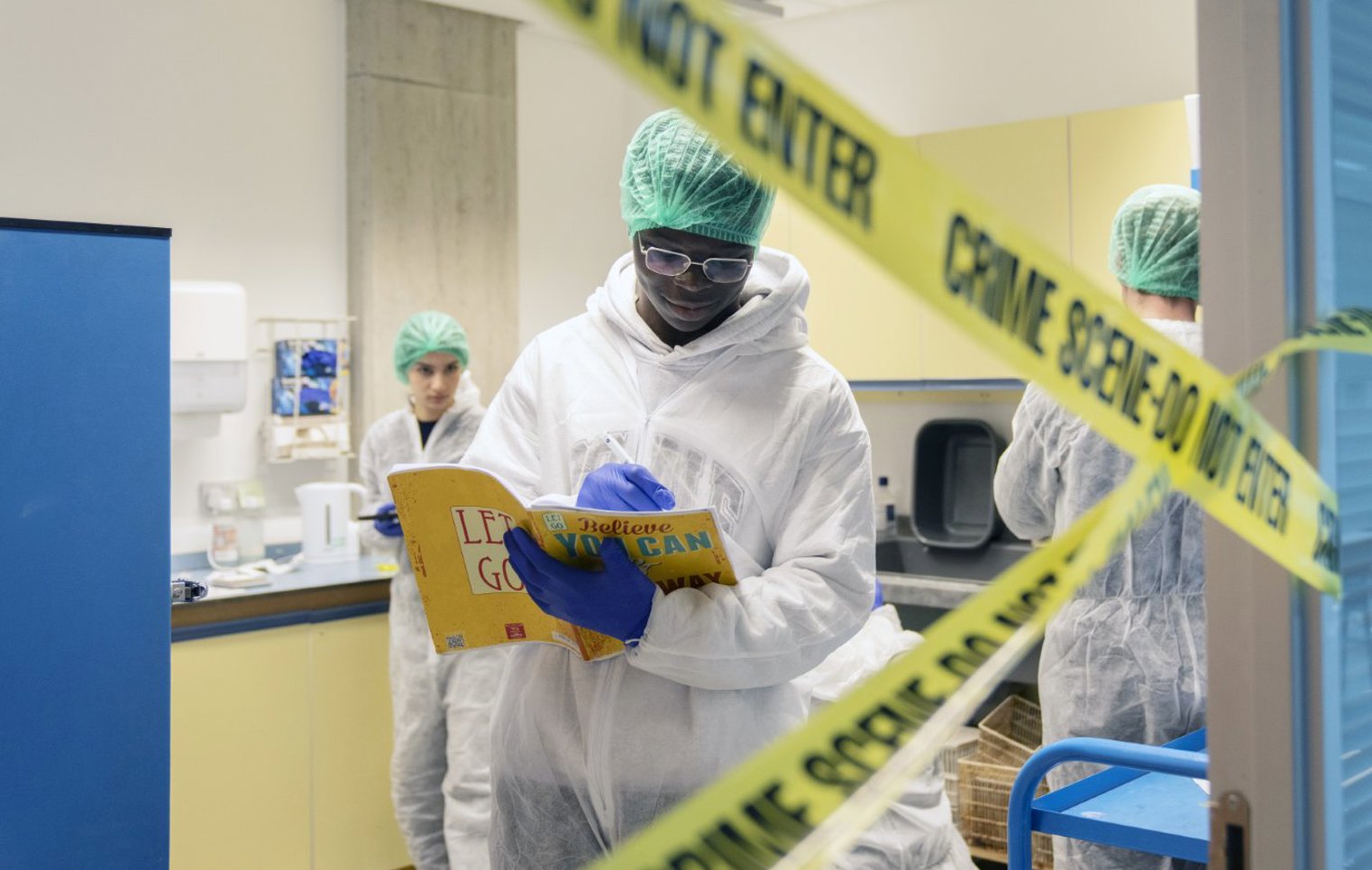 Forensic science student reads instructions behind crime scene tape during a practical lab exercise.