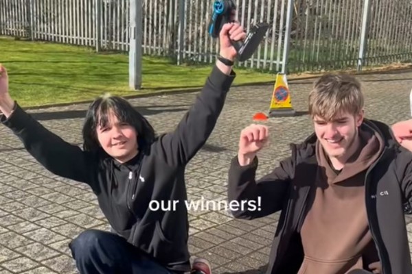 Two students celebrating after winning the Glasgow Kelvin College CAD car race, holding remote controls outdoors.