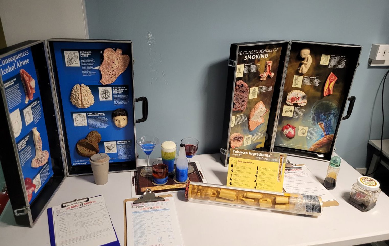 Educational display table at Glasgow Kelvin College showing the health consequences of alcohol abuse and smoking, with anatomical models, charts, and information leaflets.