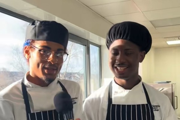 Hospitality students in chef uniforms speaking into a microphone in a professional kitchen at Glasgow Kelvin College.