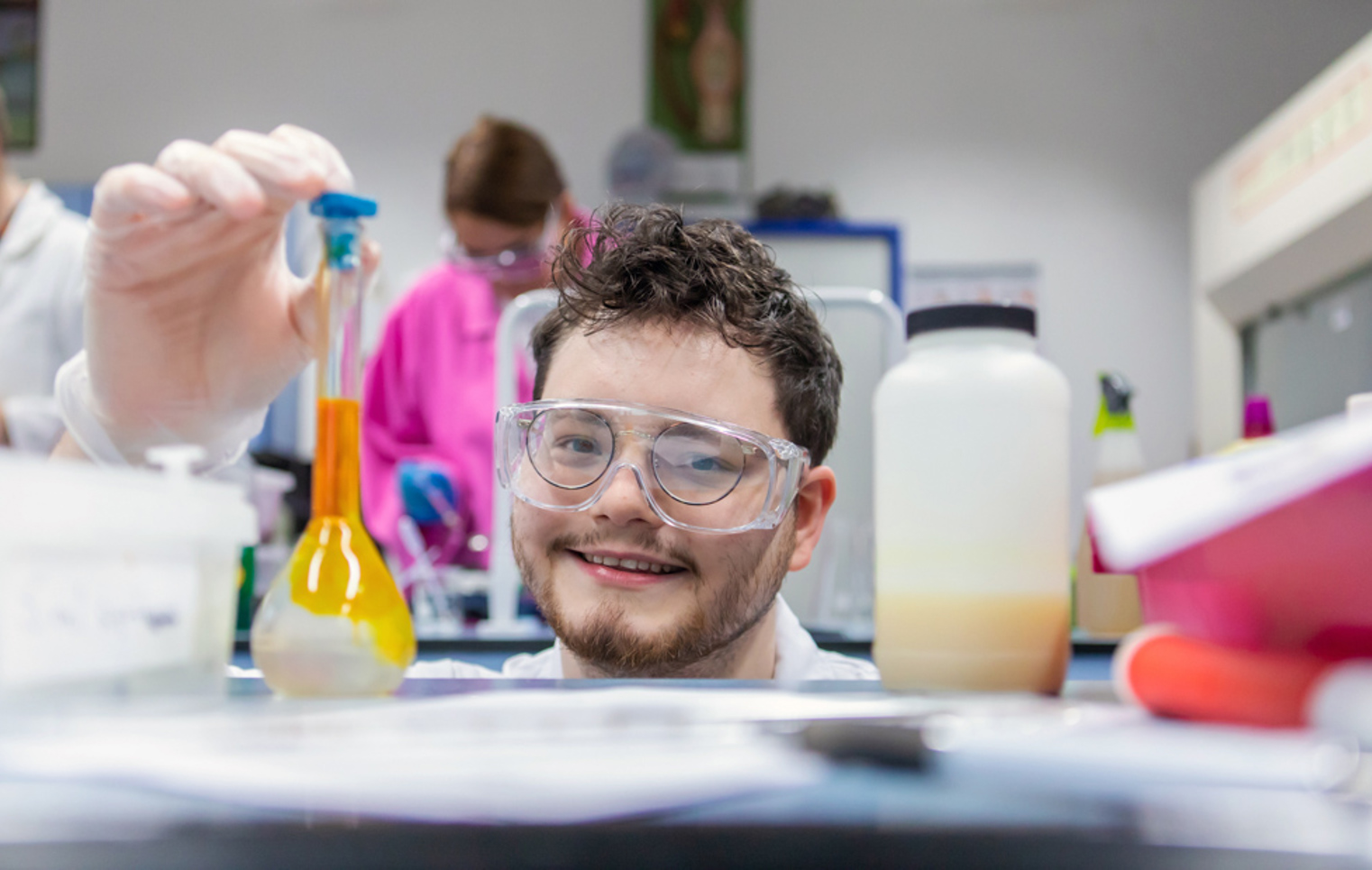 Science student smiling and holding a flask with yellow liquid in the laboratory at Glasgow Kelvin College