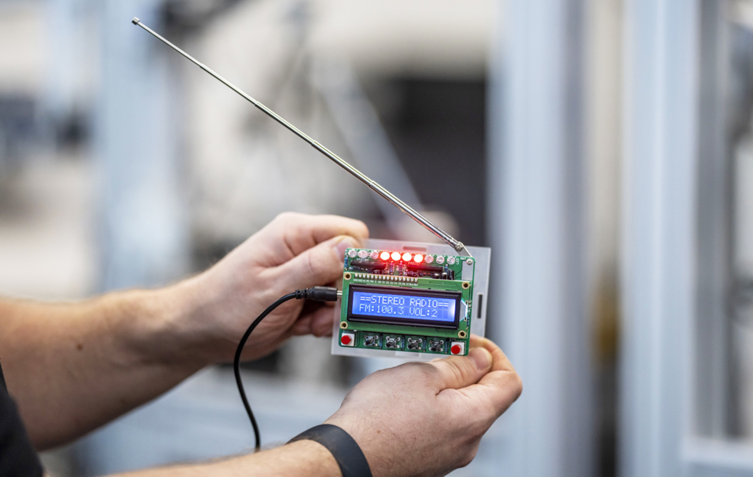 Close-up of a small electronic device with an LCD screen displaying radio frequency settings, held by a person in a technical lab.