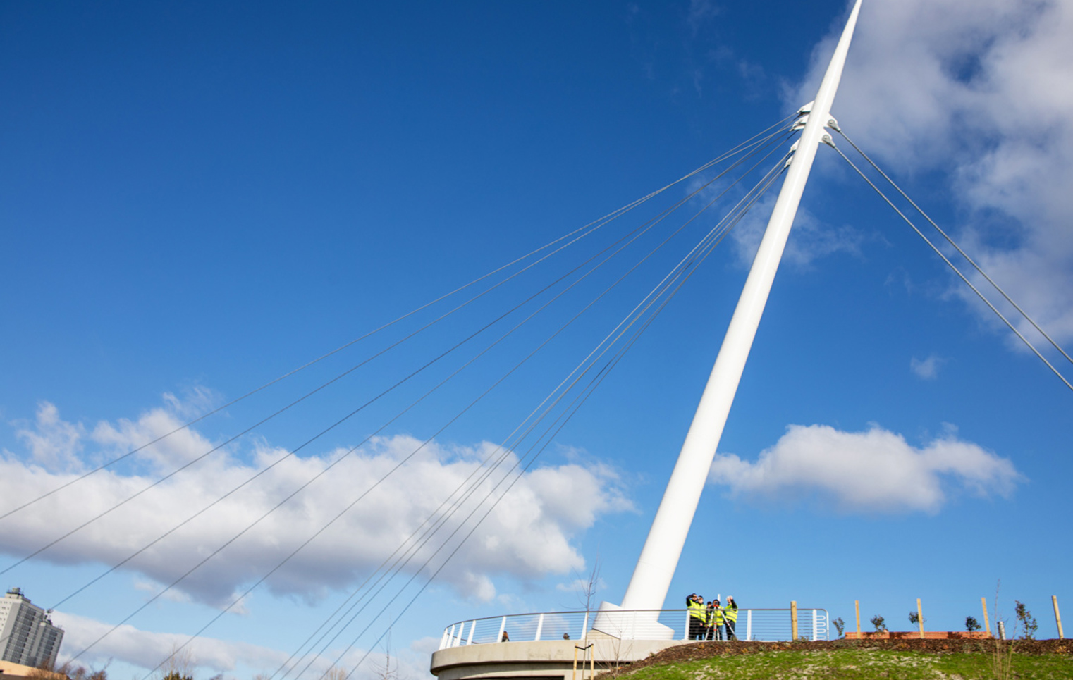 A group of civil engineering students and a lecturer in high-visibility vests conducting a land surveying exercise on the Stockingfield Bridge, viewed from a lower angle against the structure’s towering white support beam.
